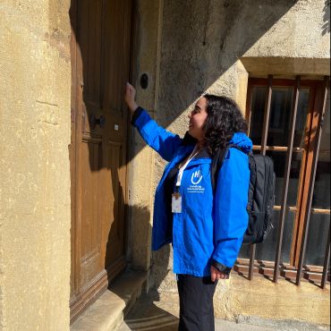 Eine Frau mit einer blauen Jacke von Handicap International beim Klopfen an eine Tür